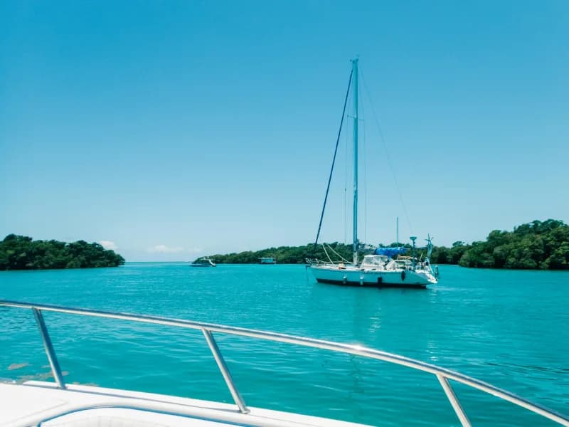 A sailboat at anchor in calm green water seen from the bow of another boat