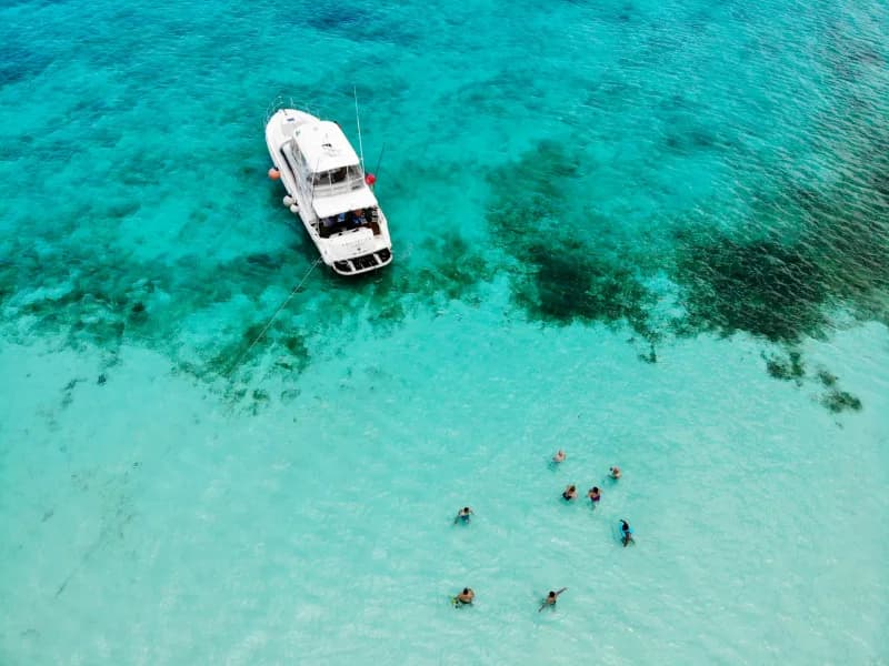 Aerial view of a white charter yacht anchored in turquoise shallows with swimmers alongside
