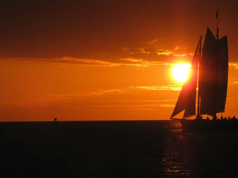 A schooner in silhouette against a deep orange Florida sunset over open water