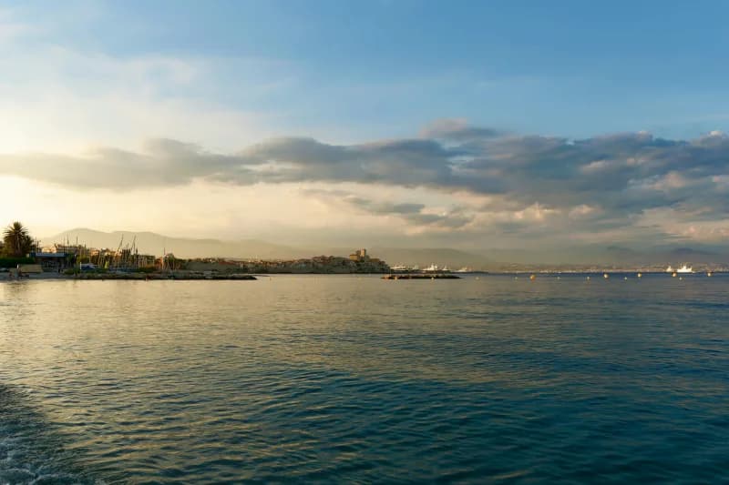 The coast at Nice seen across calm water at golden hour, with the Alps behind the town