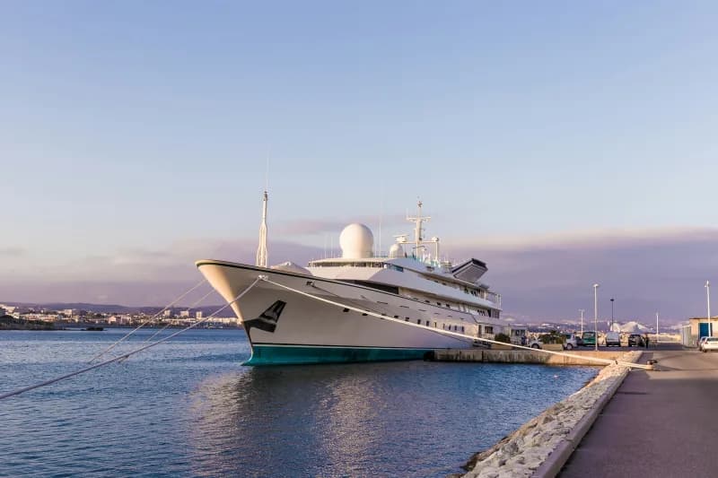 A large white superyacht moored alongside a stone quay at dusk