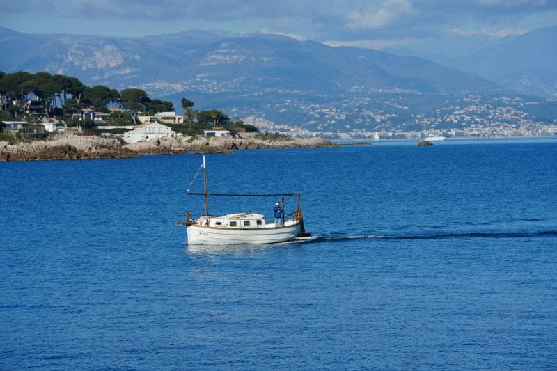 A small classic motorboat cruising along the Riviera coast with hills and villages behind