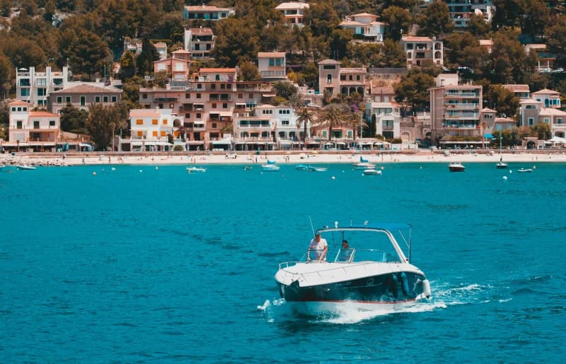 A motorboat crossing turquoise water in front of a pastel hillside village