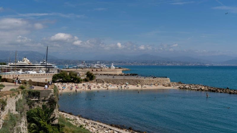 A sheltered sandy cove below the old ramparts at Antibes, with the port beyond