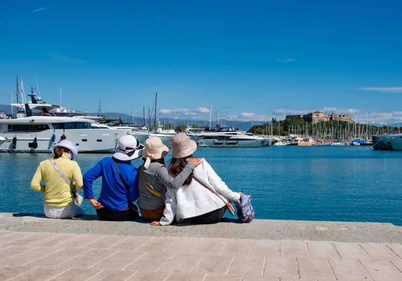 Four friends sitting on a harbour wall looking out over moored yachts